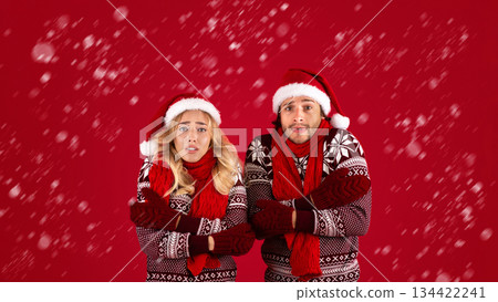 Christmas chill. Young couple in winter outfits shivering on red background, panorama Christmas chill. Young couple in winter outfits shivering on red background, panorama 134422241