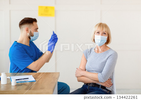 Mature woman waiting for covid-19 injection shot and young male doctor with coronavirus vaccine at health centre. Population immunization and antiviral protection campaign 134422261