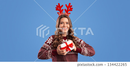 Winter holiday shopping. Pretty millennial girl in Christmas clothes holding gift box on blue background 134422265