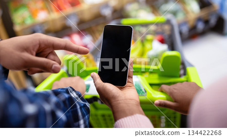 Unrecognizable black couple holding smartphone with empty screen at supermarket, mockup for your mobile app or website. African American guy and lady with cellphone shopping at mall Unrecognizable black couple holding smartphone with empty screen at supermarket, mockup for your mobile app or website. African American guy and lady with cellphone shopping at mall 134422268