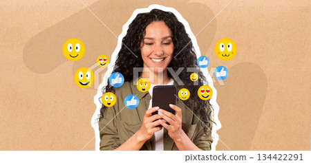 A woman with curly hair smiles while holding a smartphone, actively engaged in messaging. Colorful emojis appear around, suggesting social media interaction and enjoyment in a light-hearted setting. 134422291