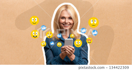 A woman smiles while holding a smartphone, engaged in lively chatting or texting. Colorful social media reaction icons surround her, highlighting her joyful communication. 134422309