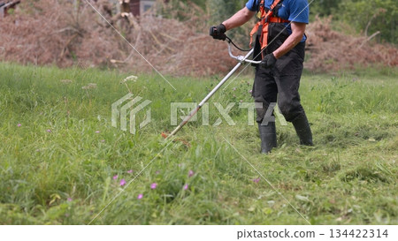 A man mows the grass with a trimmer on a summer day. A man mows the grass with a trimmer on a summer day. 134422314