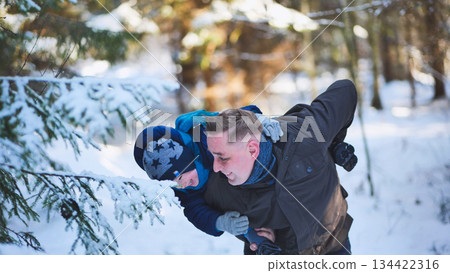 Father giving son piggyback ride, playing and having fun in beautiful snowy winter forest on sunny day 134422316