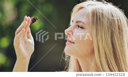 Blonde woman gently supporting delicate butterfly on fingertip, experiencing serene summer moment outdoors Blonde woman gently supporting delicate butterfly on fingertip, experiencing serene summer moment outdoors 134422328
