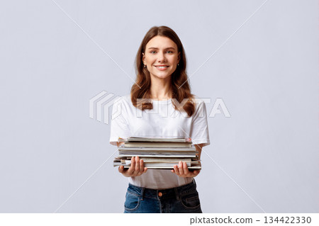 Waste Sorting. Portrait Of Beautiful Young Woman Holding Stack Of Old Magazines In Hands, Collecting Paper Garbage For Recycling, Smiling Eco-Volunteer Lady Standing Over Light Studio Background 134422330