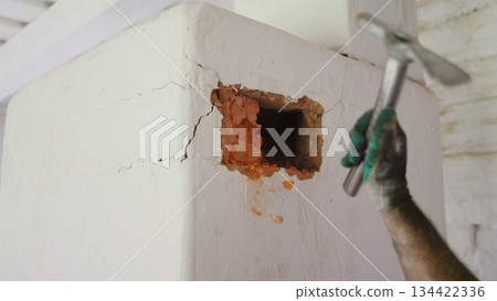 Construction worker breaking white wall with hammer revealing bricks Construction worker breaking white wall with hammer revealing bricks 134422336