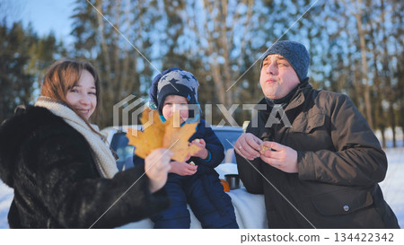 Happy family having a winter picnic, eating snacks and enjoying quality time together in a snowy forest Happy family having a winter picnic, eating snacks and enjoying quality time together in a snowy forest 134422342
