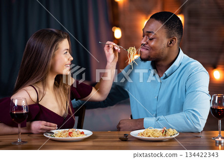 Cheerful Interracial Couple Having Fun During Romantic Dinner At Home. Young Multiracial Lovers Eating Spaghetti And Drinking Wine, Caring Woman Feeding Her Boyfriend And Smiling, Free Space Cheerful Interracial Couple Having Fun During Romantic Dinner At Home. Young Multiracial Lovers Eating Spaghetti And Drinking Wine, Caring Woman Feeding Her Boyfriend And Smiling, Free Space 134422343