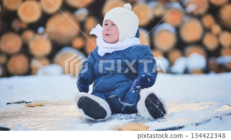 Bundled infant resting on snowy wooden surface near stacked firewood during cold winter season Bundled infant resting on snowy wooden surface near stacked firewood during cold winter season 134422348