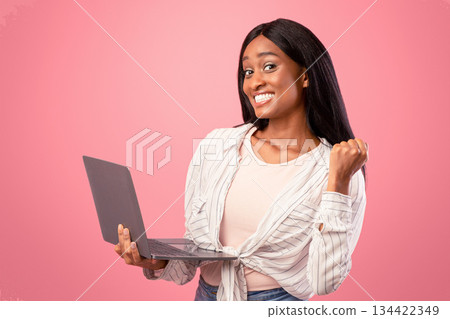 Millennial African American lady with laptop making YES gesture and smiling on pink studio background. Pretty black woman studying or working remotely, communicating online 134422349