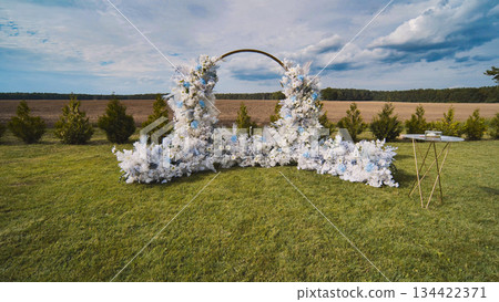 Round wedding arch decorated with white and blue flowers, ready for the ceremony in a beautiful outdoor location Round wedding arch decorated with white and blue flowers, ready for the ceremony in a beautiful outdoor location 134422371