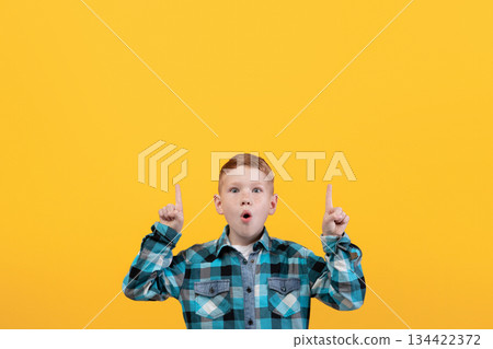 Shocked kid showing exciting advertisement, aiming at free space for text or advertisement. Surprised redhead schoolboy pointing up at empty space over yellow studio background Shocked kid showing exciting advertisement, aiming at free space for text or advertisement. Surprised redhead schoolboy pointing up at empty space over yellow studio background 134422372