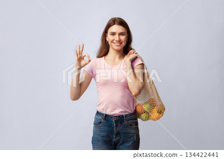 Eco Friendly Shopping. Smiling Young Woman Holding String Reusable Mesh Bag With Organic Fruits And Vegetables And Showing Ok Gesture, Positive Lady Standing On Grey Studio Background, Copy Space Eco Friendly Shopping. Smiling Young Woman Holding String Reusable Mesh Bag With Organic Fruits And Vegetables And Showing Ok Gesture, Positive Lady Standing On Grey Studio Background, Copy Space 134422441