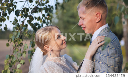 Loving newlyweds embracing beneath birch tree, wedding attire highlighting romantic connection and intimate celebration Loving newlyweds embracing beneath birch tree, wedding attire highlighting romantic connection and intimate celebration 134422459