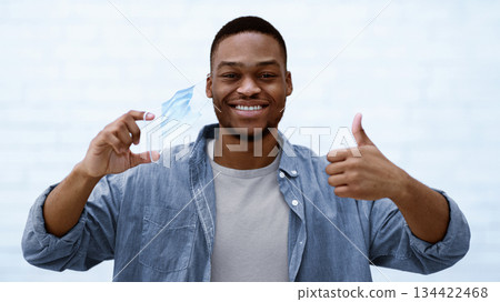 End Of Coronavirus Pandemic. Happy Black Guy Taking Off Face Mask Gesturing Thumbs Up Over White Background. Covid-19 Recovery, Corona Vaccination And Successful Medical Treatment Concept End Of Coronavirus Pandemic. Happy Black Guy Taking Off Face Mask Gesturing Thumbs Up Over White Background. Covid-19 Recovery, Corona Vaccination And Successful Medical Treatment Concept 134422468