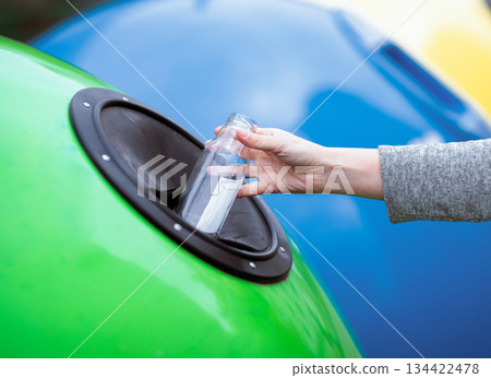 Hand throwing empty glass bottle into yellow recycle bin container outdoors, unrecognizable woman enjoying waste sorting ang garbage recycling, cropped image with selective focus, closeup Hand throwing empty glass bottle into yellow recycle bin container outdoors, unrecognizable woman enjoying waste sorting ang garbage recycling, cropped image with selective focus, closeup 134422478