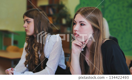 Two high school girls are sitting at desks in a classroom, listening to a lecture or presentation 134422493