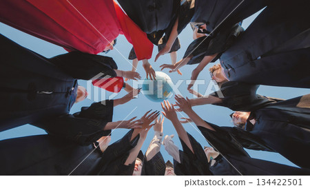 Graduates in academic gowns reaching for a globe, representing their global ambitions and unity in a diverse world Graduates in academic gowns reaching for a globe, representing their global ambitions and unity in a diverse world 134422501