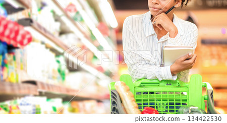Concerned Black Lady Thinking Buying Food And Calculating Increased Food Prices Standing In Supermarket, Having Financial Issues During Crisis. Discontented Female Buyer In Food Shop. Empty Space 134422530