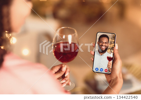 Celebrating Anniversary. Back over the shoulder view of young black woman having a romantic online date with her man, holding glass of red wine and mobile phone, toasting. Stay Safe At Home 134422540