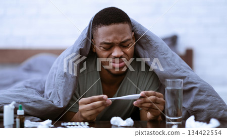 Sick Black Man Holding Thermometer Having Fever Symptom Lying In Bed At Home. African Guy Having Flu Measuring Body Temperature. Covid-19, Coronavirus And Influenza Illness. Selective Focus 134422554
