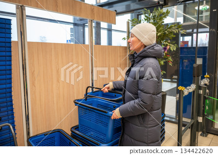Woman taking shopping basket at supermarket entrance during winter season 134422620