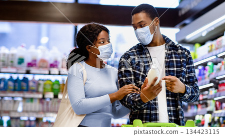 Young black couple in protective masks shopping for food together at supermarket during covid lockdown. Millennial African American woman and her boyfriend choosing fresh products at mall 134423115
