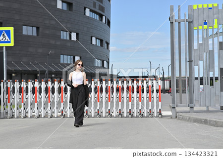 Woman walking near a retractable barrier with a modern building in the background. Woman walking near a retractable barrier with a modern building in the background. 134423321