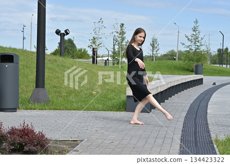 Woman balancing barefoot outdoors on a park pathway on a sunny day. Woman balancing barefoot outdoors on a park pathway on a sunny day. 134423322