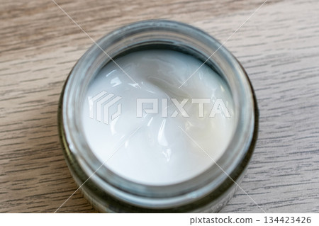 Open Jar of White Skincare Cream on a Wooden Surface 134423426