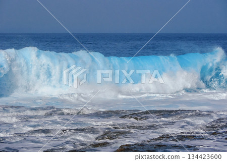 Powerful Blue Ocean Wave Breaking on Rocky Shore 134423600