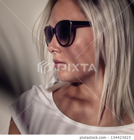Stylish woman wearing sunglasses with soft shadow overlay on a neutral background 134423823