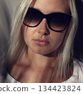 Blonde Woman Wearing Sunglasses With Shadows on Her Face Indoors 134423824
