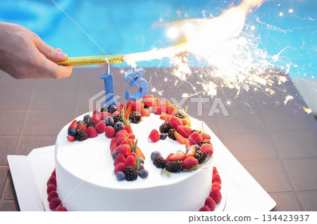 White cream cake with red berries and the number thirteen with fireworks 134423937