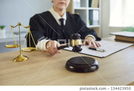 Female judge, wearing robe, holding gavel in legal office, scales of justice, document, court 134423950