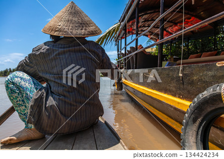Local Woman Paddling Traditional Canoe by a Cruise Boat Mekong Delta, Vietnam Local Woman Paddling Traditional Canoe by a Cruise Boat Mekong Delta, Vietnam 134424234