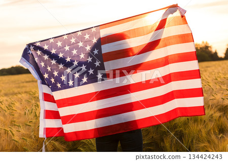 Silhouette of Young Woman Holding USA Flag in Field at Sunset 134424243