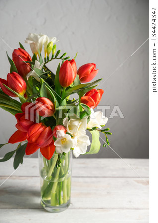 Spring floral background. Red tulips and Fresia white flower bouquet in glass vase. Copy space 134424342