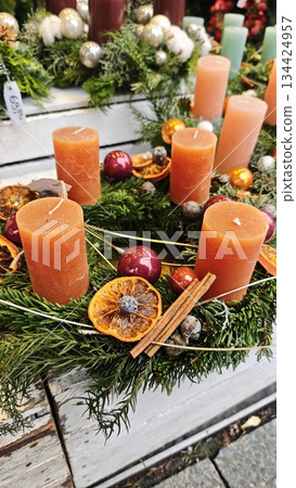 Christmas wreath with orange candles, dried citrus slices, cinnamon sticks and baubles on evergreen branches. Concept of warm holiday aroma, natural beauty and traditional seasonal charm Christmas wreath with orange candles, dried citrus slices, cinnamon sticks and baubles on evergreen branches. Concept of warm holiday aroma, natural beauty and traditional seasonal charm 134424957