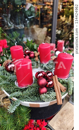 Christmas wreath with red candles, baubles, pine branches and cinnamon sticks arranged in a festive display. Concept of warm holiday tradition, Advent symbolism and cozy seasonal atmosphere Christmas wreath with red candles, baubles, pine branches and cinnamon sticks arranged in a festive display. Concept of warm holiday tradition, Advent symbolism and cozy seasonal atmosphere 134424962