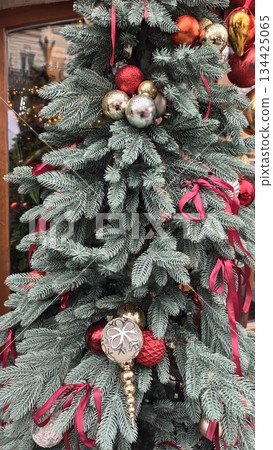 Frosted pine branches decorated with red ribbons and metallic Christmas ornaments create a festive winter look. Concept of holiday elegance, seasonal charm and traditional Christmas decor 134425065