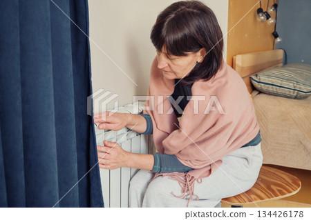 Woman feeling cold pressing hands against room radiator for warmth 134426178