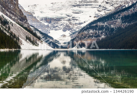 Majestic view of Lake Louise green lake reflecting snow-capped mountains and evergreen forests under cloudy sky in Banff National Park, Canada 134426190
