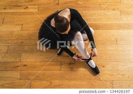 Ballerina puts on pointe shoes on leg in dance class. Classical ballet dancer woman in dance studio. Ballerina putting on tying classical pointe shoes for dance training. Ballet school concept 134426197