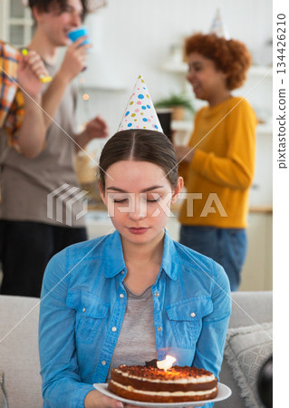 Sad lonely frustrated unhappy young woman looking at birthday cake with candle on birthday party. Girl sad disappointed thinking about life. Birthday party with friends. People celebrating birthday 134426210
