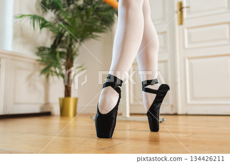 Ballerina stretching practicing ballet positions dancing near ballet barre in dance class. Legs with pointe shoes close up. Classical dancer woman in dance studio. Ballet class training Ballet school Ballerina stretching practicing ballet positions dancing near ballet barre in dance class. Legs with pointe shoes close up. Classical dancer woman in dance studio. Ballet class training Ballet school 134426211