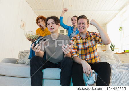 Home party. Cheerful group of friends playing video games at home. Happy diverse group buddies having fun together indoor. Friendship leisure entertainment concept. Young best friends enjoying weekend Home party. Cheerful group of friends playing video games at home. Happy diverse group buddies having fun together indoor. Friendship leisure entertainment concept. Young best friends enjoying weekend 134426225
