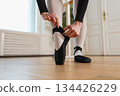 Ballerina puts on pointe shoes on leg in dance class. Classical ballet dancer woman in dance studio. Ballerina putting on tying classical pointe shoes for dance training. Ballet school concept 134426229