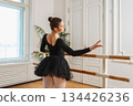 Young ballerina in tutu skirt stretching practicing ballet positions dancing near ballet barre in dance class. Young classical dancer woman in dance studio. Ballet class training Ballet school concept 134426236